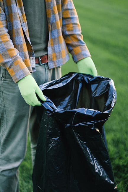 A black wheeled rubbish bin with a white label and the words 'ST. JOHN'S' printed on the front is positioned on a sidewalk next to a curb in a residential area during nighttime. The lid of the bin is